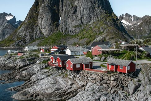 Traditional red rorbuer (fishermen’s cabins) in Hamnøy, Lofoten, Norway, with dramatic mountain peaks rising behind the village.