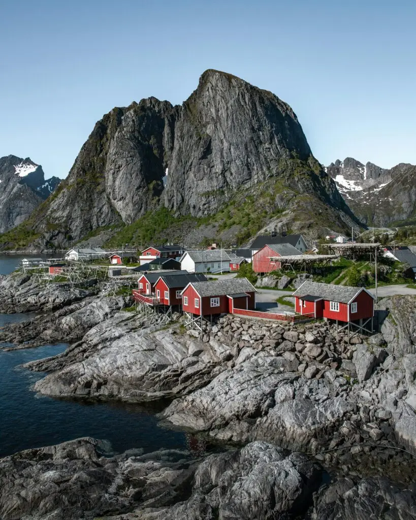 Traditional red rorbuer (fishermen’s cabins) in Hamnøy, Lofoten, Norway, with dramatic mountain peaks rising behind the village.