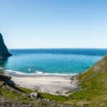 Scenic view of Kvalvika Beach in Lofoten, Norway, surrounded by steep mountains and the turquoise waters of the Norwegian Sea, as seen from the hiking trail.