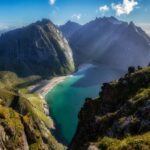 Stunning view of Kvalvika Beach from the Ryten hiking trail in Lofoten, Norway, showcasing turquoise waters, white sand, and towering mountain cliffs.