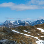Snowy mountain peaks seen from Tuva summit in Lofoten with red-marked trail pole in foreground