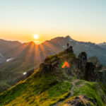 Hiker standing on ridge of Blåtinden in Lofoten with glowing sunset over mountain peaks and valleys