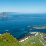 Hiker standing on Nordlandsnupen with panoramic views over Mosken, white beaches, and turquoise sea.