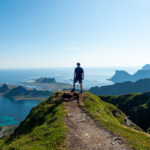 Hiker standing on the summit of Nordlandsnupen, overlooking Værøy and the surrounding sea.