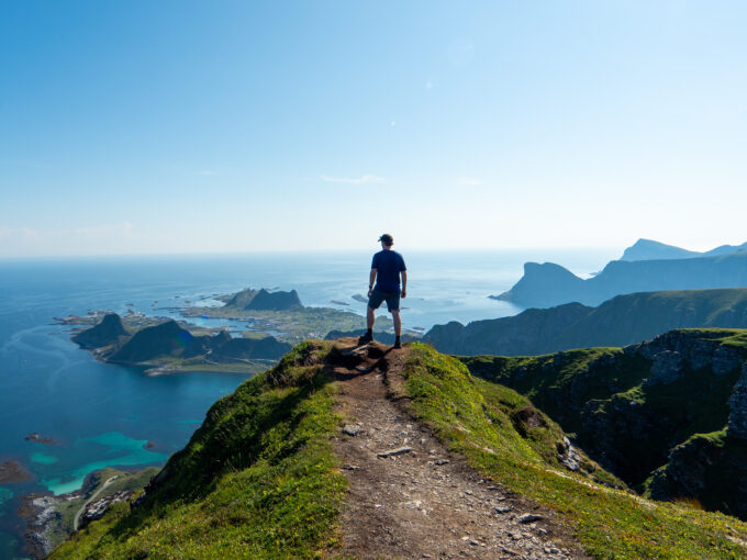 Hiker standing on the summit of Nordlandsnupen, overlooking Værøy and the surrounding sea.