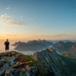Man watching sunset over Lofoten mountain peaks from the top of Moltinden, Norway.