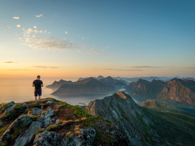 Man watching sunset over Lofoten mountain peaks from the top of Moltinden, Norway.